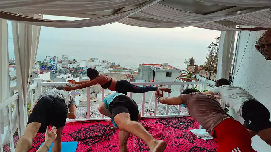 A group of people practicing yoga in Taghazout in a terrace with sea view.
