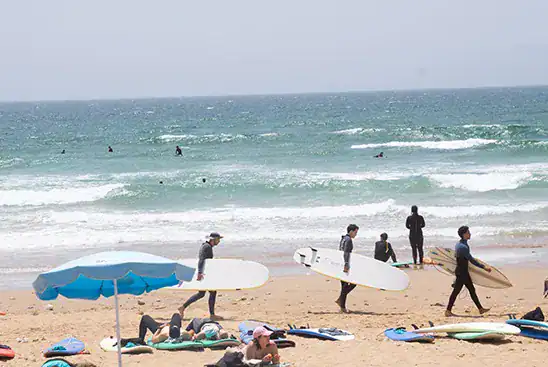 People sunbathing and surfers walking at the beach in Taghazout.