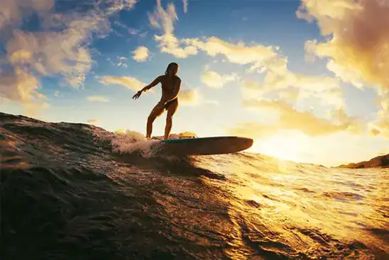 A woman surfing riding a wave at sunset in Taghazout.