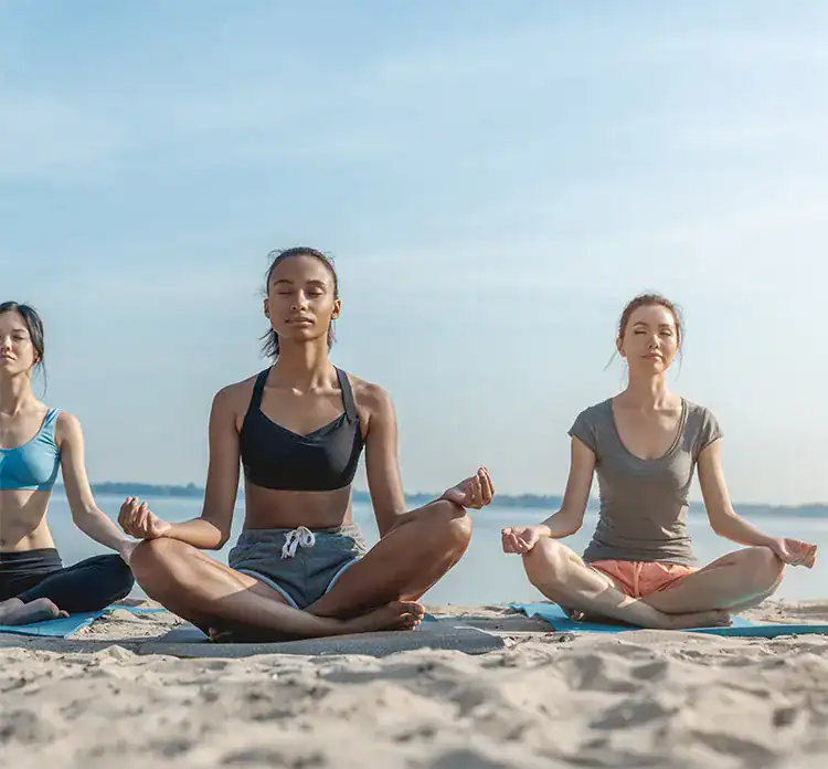 Three women meditating at the beach in Taghazout.