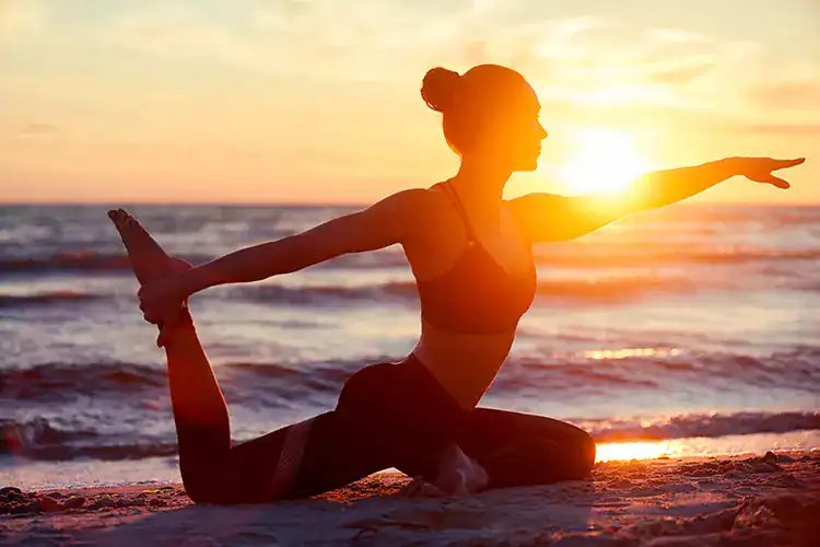 A woman practicing yoga ath the beach by sunset in Taghazout.