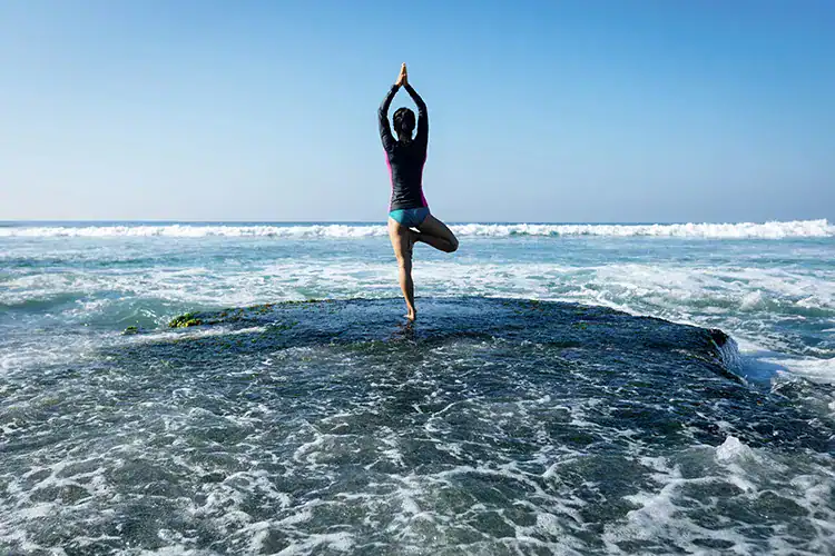 A woman practicing yoga in Taghazout on the rocks by the ocean in Taghazout.